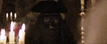 a statue of a man wearing a black mask and a hat is in front of candles .