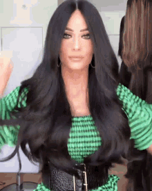 a woman with long black hair is wearing a green and black striped dress and a black belt .