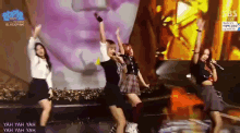 a group of girls are dancing on a stage with a statue in the background