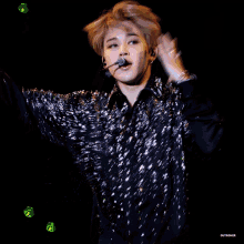 a man wearing a black sequined jacket is on a stage
