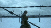 a soldier is walking through a snowy field with barbed wire behind him