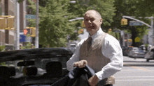 a man in a white shirt and tan vest is walking down a street