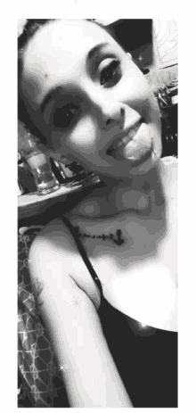 a woman with a tattoo on her shoulder is sticking her tongue out in a black and white photo .