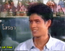 a man in a white shirt is smiling in front of a sign that says lk fan on it