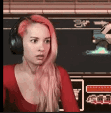 a woman with pink hair is wearing headphones and making a surprised face .