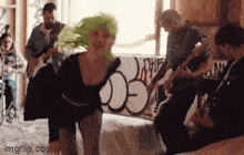 a woman with green hair is dancing in front of a group of people playing instruments