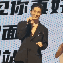 a man in a suit is holding a microphone and smiling while standing in front of a sign with chinese characters .