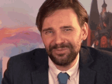 a man with a beard wearing a suit and tie looks at the camera