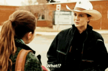 a woman in a cowboy hat is talking to another woman and says " what "