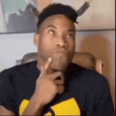 a man wearing a black shirt with a yellow wu tang logo on it is thinking about something .