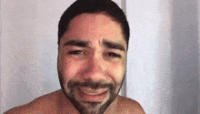 a shirtless man with a beard is crying while looking at the camera .