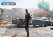 a man in a spiderman costume is standing in a parking lot next to cars .