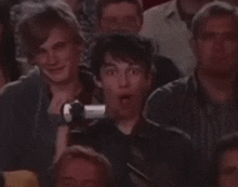 a group of people are sitting in a theater and one of them is holding a camera over his face
