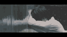 a man in a white shirt is leaning against a wall with his head down