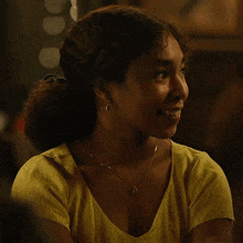 a woman wearing a yellow shirt and a necklace is smiling