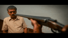 a man with a mustache looks at a person holding a gun