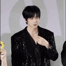 a young man in a black sequined jacket is standing in front of a white background .