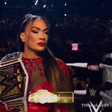 a woman in a red dress is holding a wrestling championship belt in front of a crowd