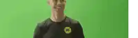 a man wearing a black shirt with a yellow k on it is smiling in front of a green background .