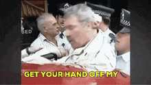 a man is being held by a group of police officers with the words get your hand off my