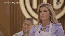 a woman in a purple shirt and white apron is sitting in front of a masterchef logo