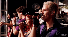 a group of people singing into microphones with rbd.gif in the lower right corner