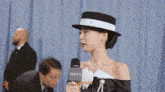 a woman in a hat is holding a microphone in front of a man in a suit .