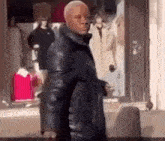 a man in a black coat is standing in front of a store window .