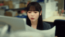 a woman sitting at a desk looking at a computer monitor