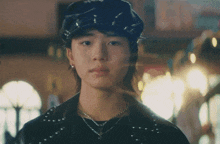 a young man wearing a hat and a necklace is looking at the camera .