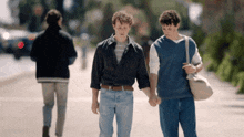 two young men holding hands while walking down a street