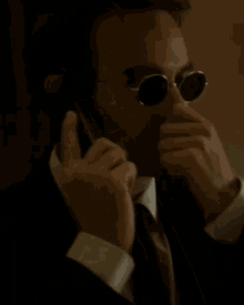 a man in a suit and tie wearing sunglasses is smiling while talking on a cell phone