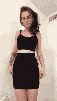 a woman wearing glasses and a black crop top is standing in front of a white wall