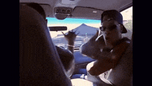 a man wearing sunglasses and a baseball cap is sitting in a car talking to another man