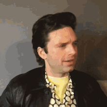 a man wearing a black jacket and a yellow shirt is making a face .
