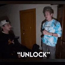 two young men are standing next to each other in a dark room and one of them is wearing a blue tie dye sweatshirt .