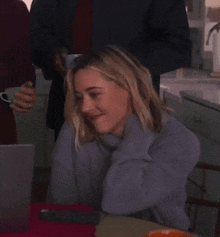 a woman in a grey sweater is sitting at a table in front of a laptop .