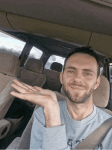 a man with a beard is sitting in the back seat of a car with his hand out