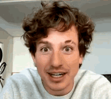 a man with curly hair is making a funny face while wearing a gray sweater .
