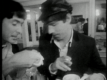 a black and white photo of two men eating food