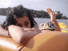 a woman in a bikini is laying on a yellow raft in the water with the word tropic in the corner