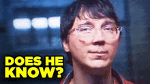 a man with glasses and a scar on his face is looking at the camera with the words `` does he know '' behind him .