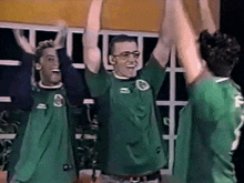 three men wearing green shirts with the number 2 on the back are raising their arms in the air