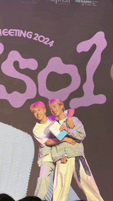 two people hugging in front of a sign that says 2024