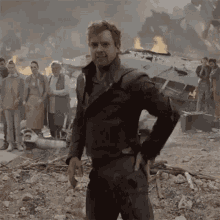 a man in a suit is standing in front of a group of people in a destroyed city .