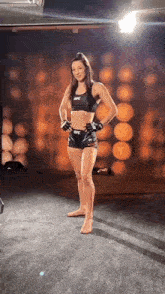 a woman in a crop top and shorts is standing on a wrestling mat in a gym .