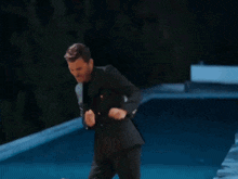 a man in a suit is dancing in front of a swimming pool