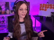 a woman wearing headphones and glasses is pointing at something in front of a sign that says cat shop on it