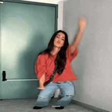 a woman in a red shirt and jeans is dancing in front of a door