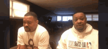a man wearing a hoodie that says osos hat2 ua is sitting next to another man